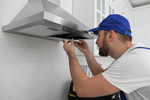 Un profesional de control de plagas comprobando si hay cucarachas en la campana extractora.